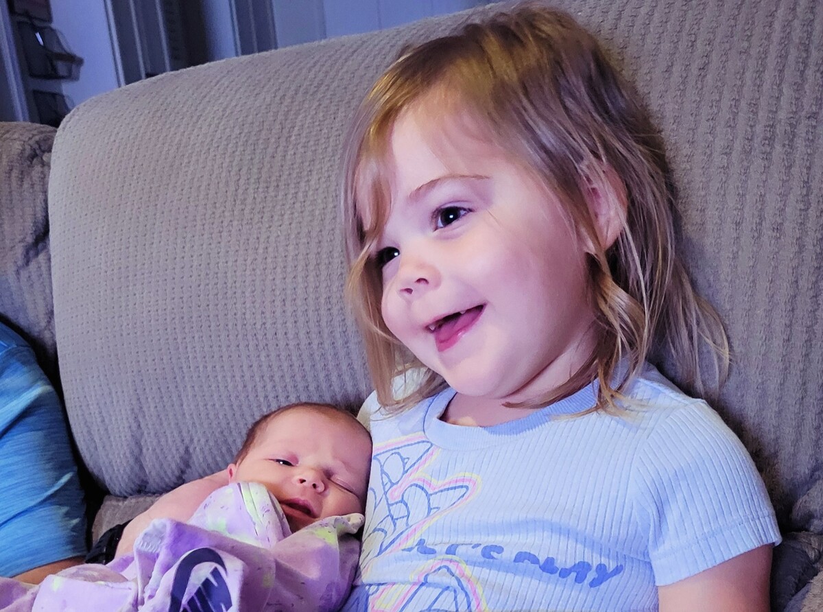 A young girl smiles while holding a swaddled baby